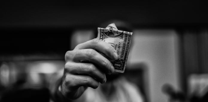 A man holds a bundle of folded dollar bills close to the camera, obscuring his face