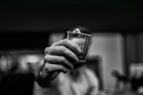 A man holds a bundle of folded dollar bills close to the camera, obscuring his face