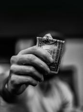 A man holds a bundle of folded dollar bills close to the camera, obscuring his face